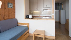 A compact living space with a kitchenette, a wooden bench, and a small table. - 2-Room Apartment, Near Slopes, Balcony and Free Wifi (Tignes)