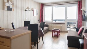 A cozy living room with a sofa, a dining table, and a small table. There is a window with curtains and a radiator. - South/West Apt 2R, 500m from slopes, Wi-Fi, Val-Claret (Tignes)