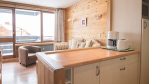 Una habitación acogedora con suelo de madera, un sofá, una mesa de comedor y una zona de cocina con cafetera y microondas.