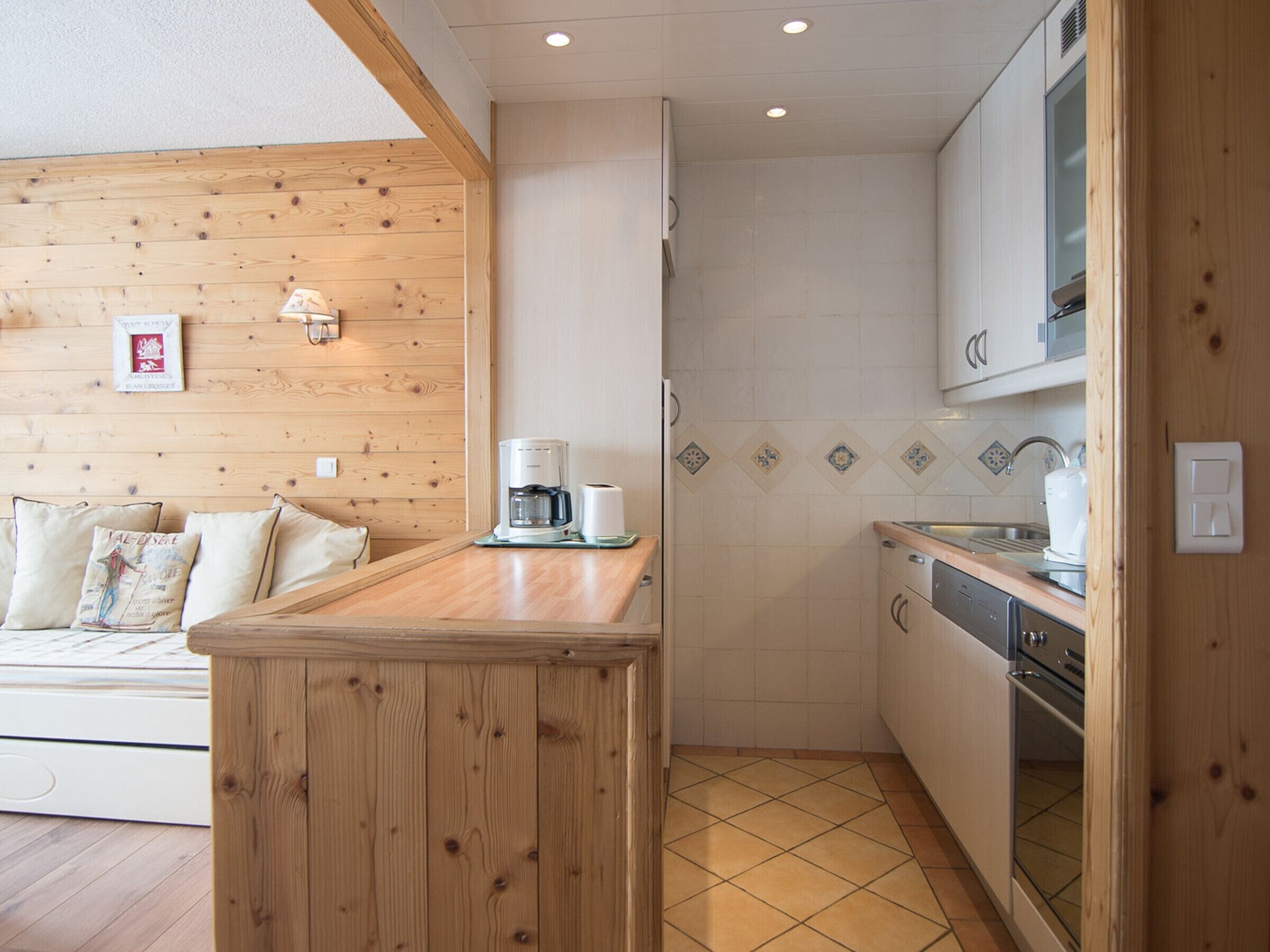 A compact kitchen with wooden cabinetry, a coffee maker, and a tiled backsplash.