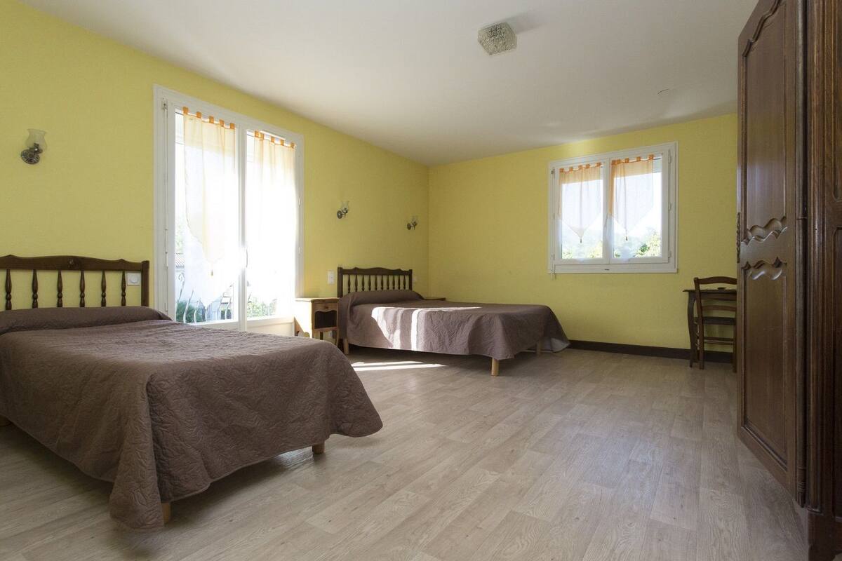 Une chambre avec deux lits, des têtes de lit en bois, une armoire et une fenêtre avec des rideaux.