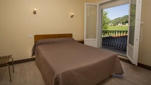 A bedroom with a bed, a wooden bench, and a sliding glass door leading to a balcony with a view of a green landscape. - Hotel Espellet (Larceveau-Arros-Cibits)