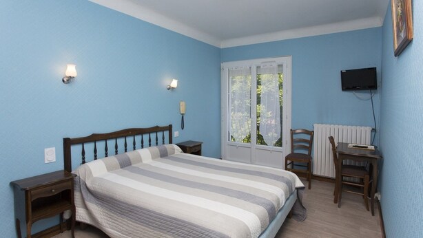 A bedroom with a bed, bedside tables, a chair, a desk, a television, and a window with a view of greenery. - Hotel Espellet (Larceveau-Arros-Cibits)