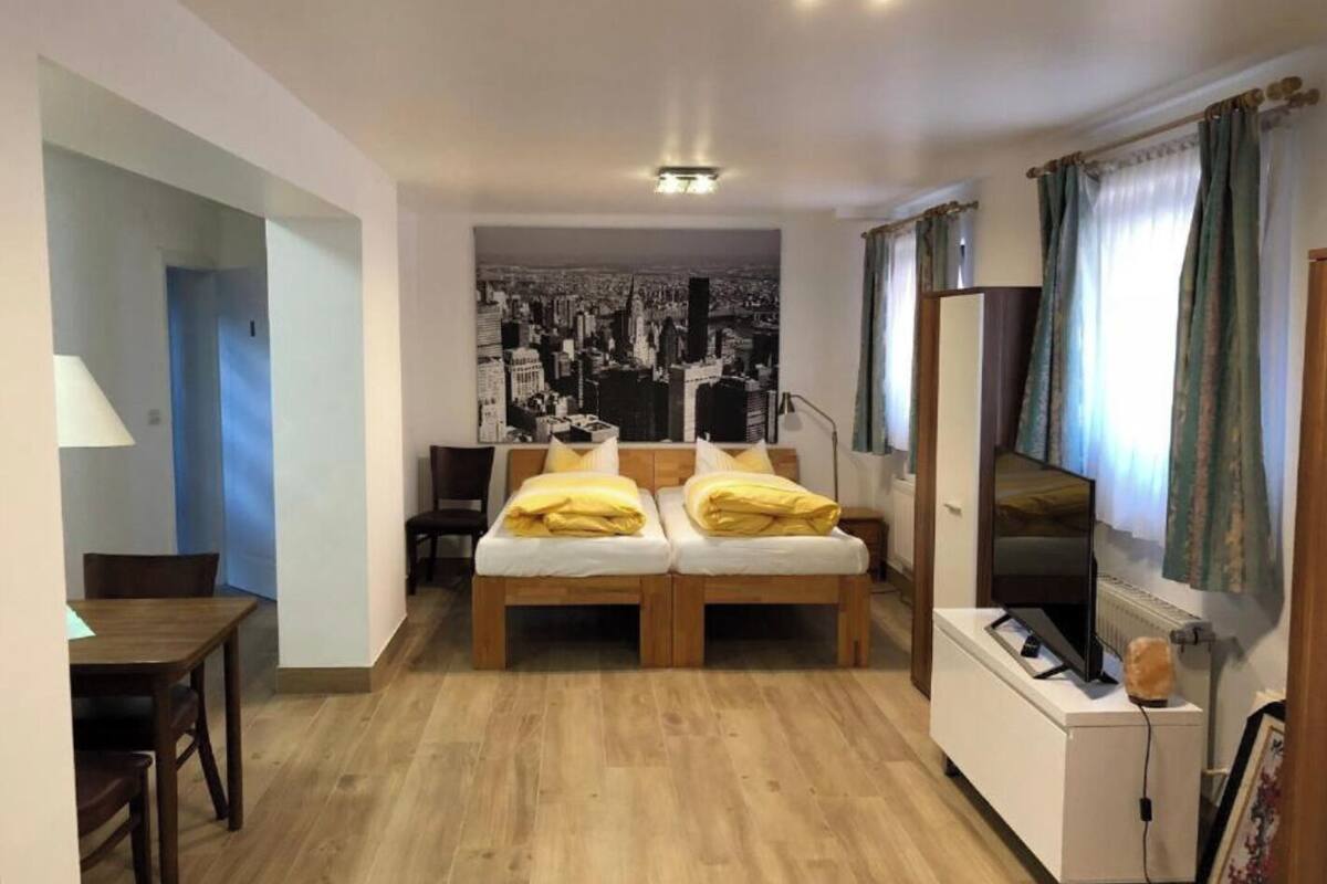 A compact room with a bed, a desk, and a chair. There is a cityscape poster on the wall and a window with curtains.