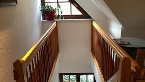 Una escalera de madera con barandilla que conduce a un rellano con una ventana y una puerta.