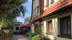 Un estrecho camino adoquinado flanqueado por edificios de arquitectura tradicional, incluyendo uno con toldo rojo y un cartel que indica restaurante.