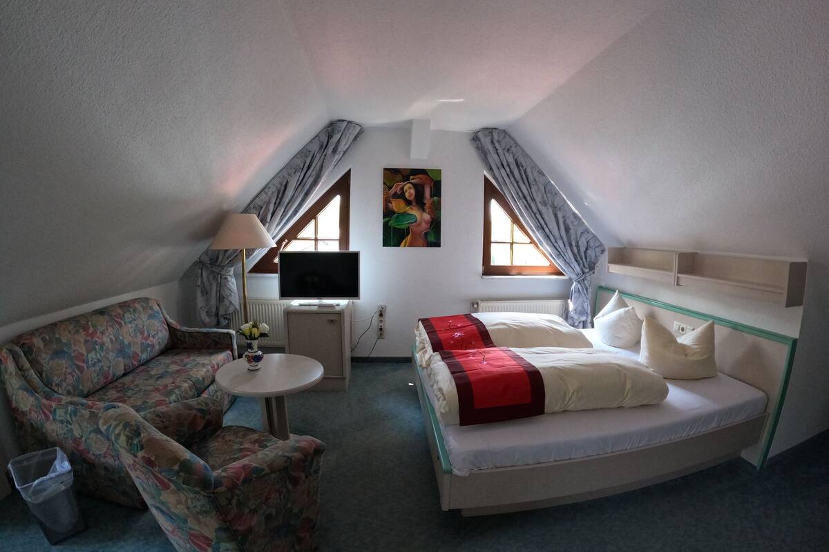 A small, cozy room with a sofa, a bed, a TV, and a small table with a lamp.