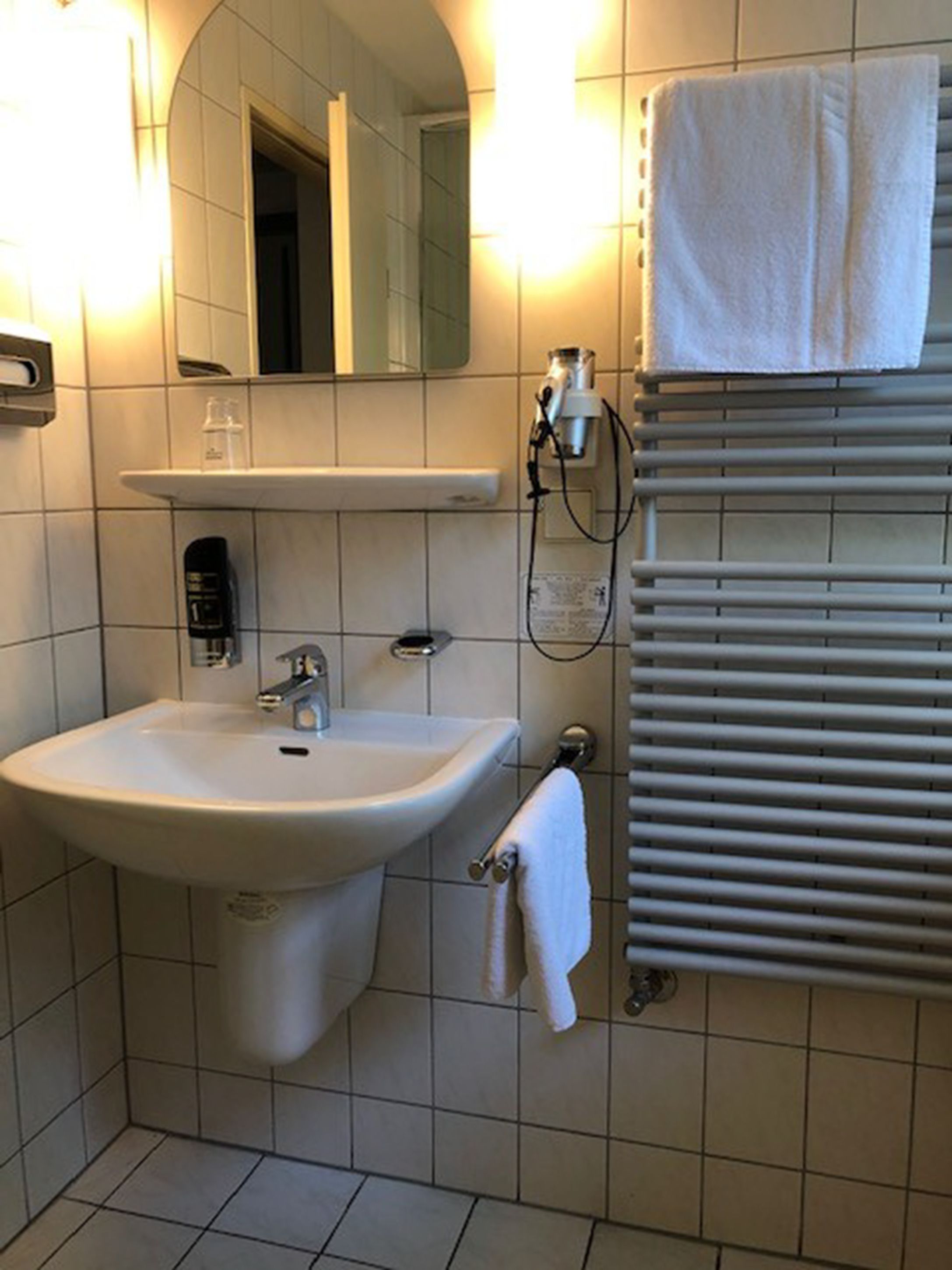 A bathroom with a sink, mirror, towel rack, and towel warmer.