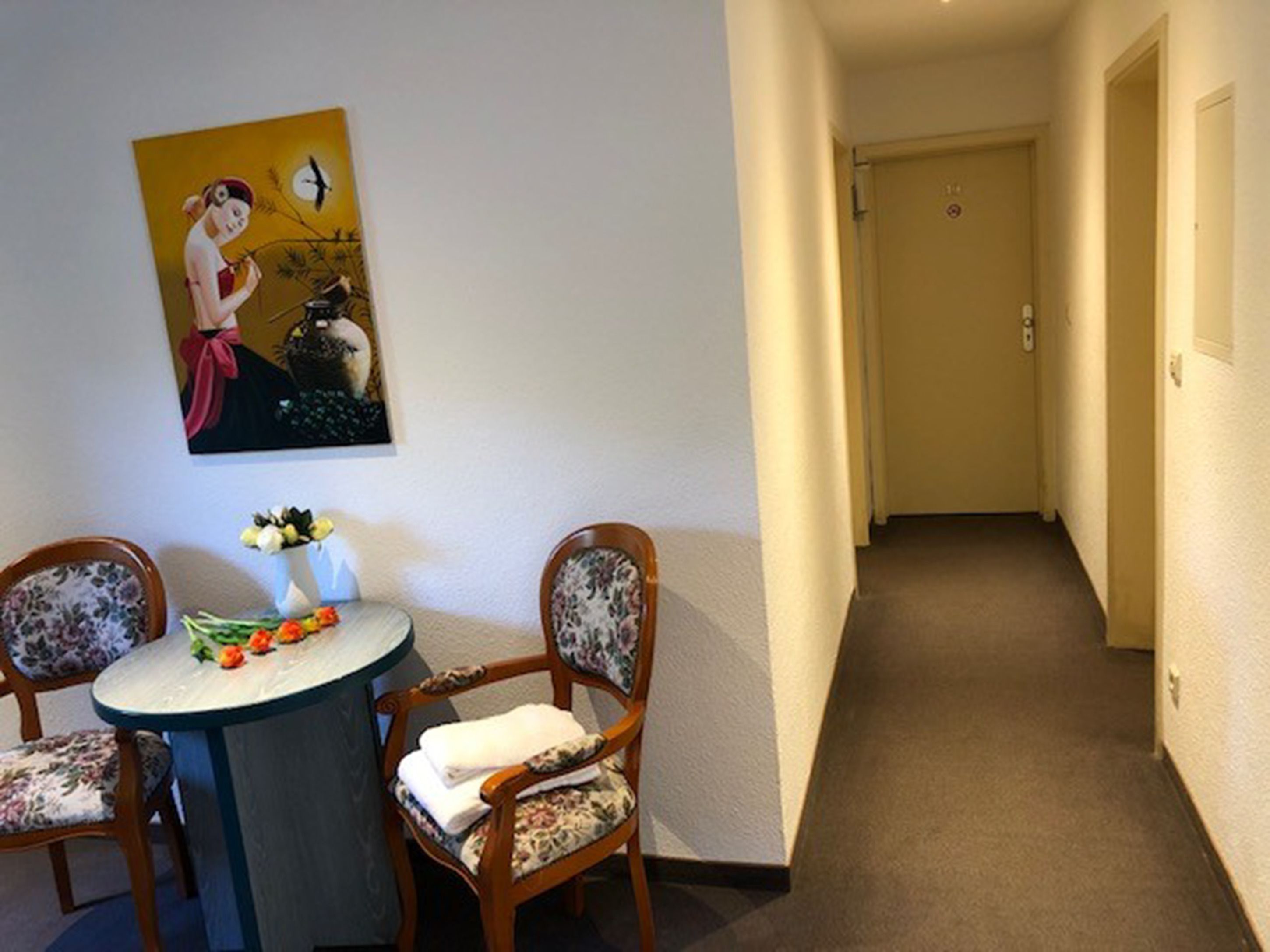 A hallway with a door at the end, a round table with chairs, and a painting on the wall.