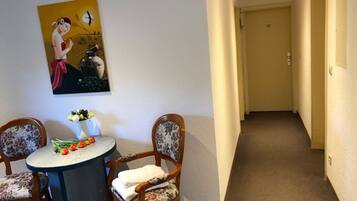 A hallway with a door at the end, a round table with chairs, and a painting on the wall.