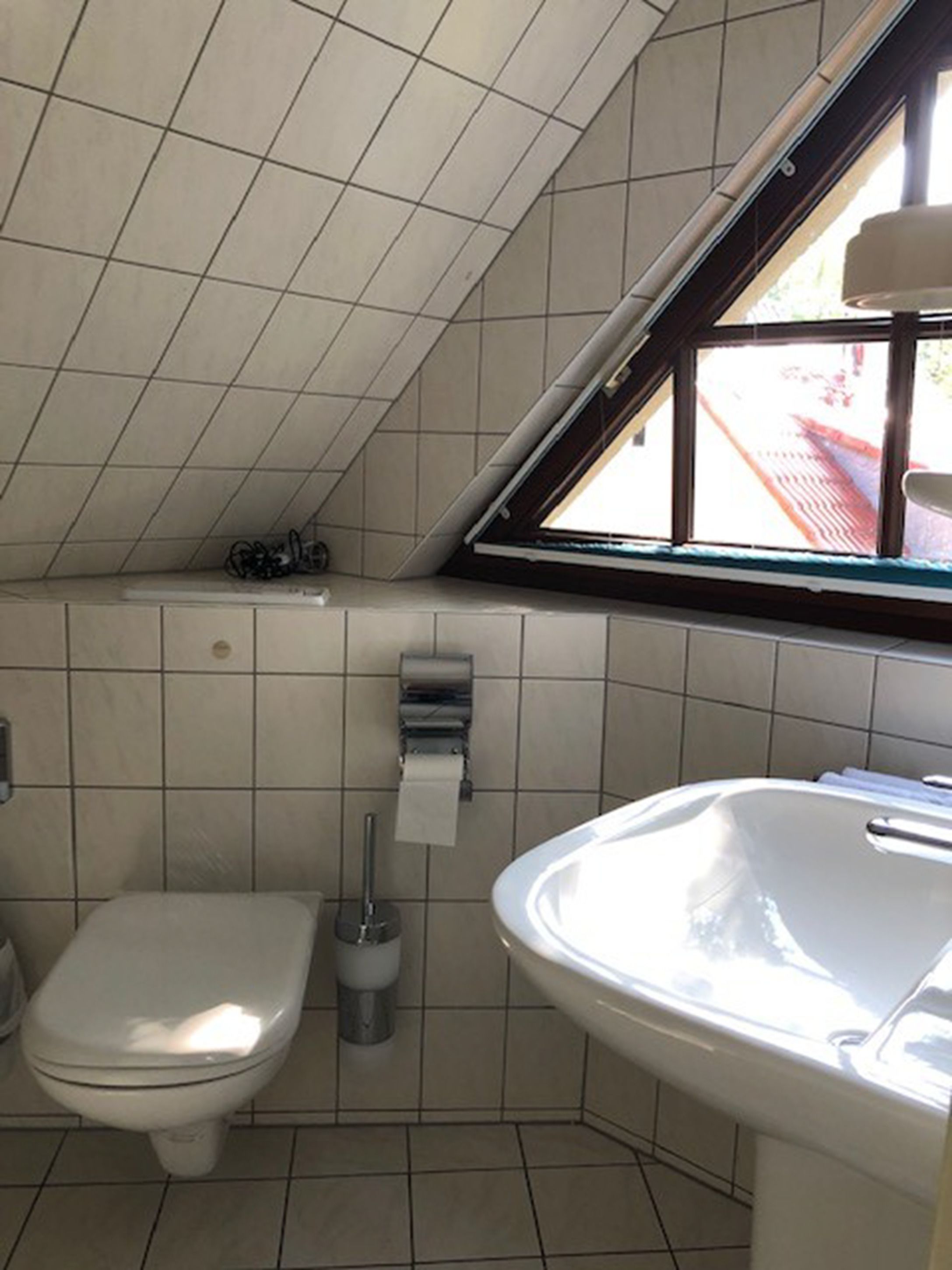 A small bathroom with a toilet, a sink, and a window.