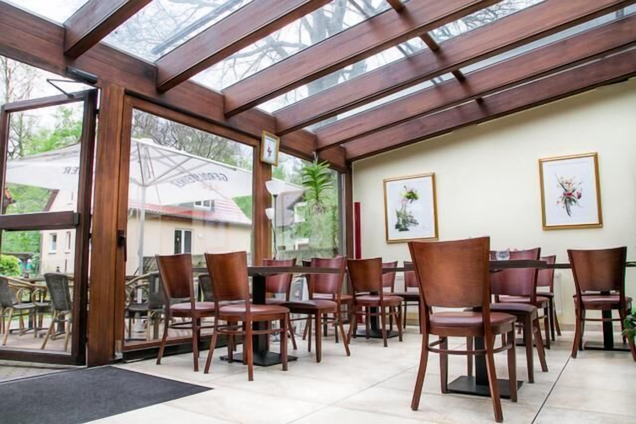 Un restaurante con sillas y mesas de madera, ventanas amplias y obras de arte enmarcadas en las paredes.