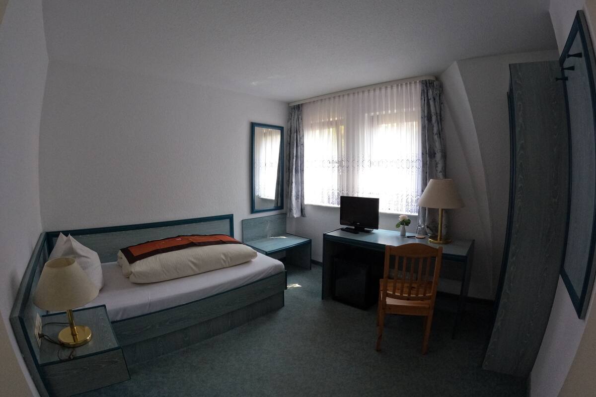 A hotel room with a bed, a desk, a chair, a TV, and a window with curtains.