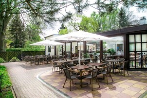 An outdoor patio with tables and chairs, surrounded by trees and a brick pathway.