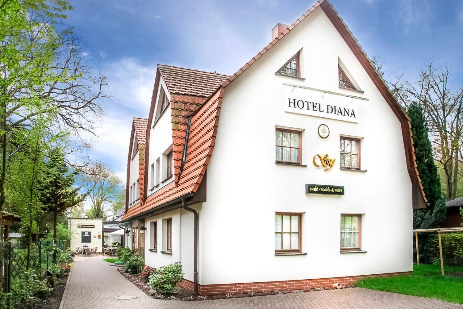 Ein weißes Gebäude mit einem Schild, auf dem „HOTEL DIANA“ steht, und einem kleineren Schild darunter mit der Aufschrift „Sushi – Nudeln und Tofu“.