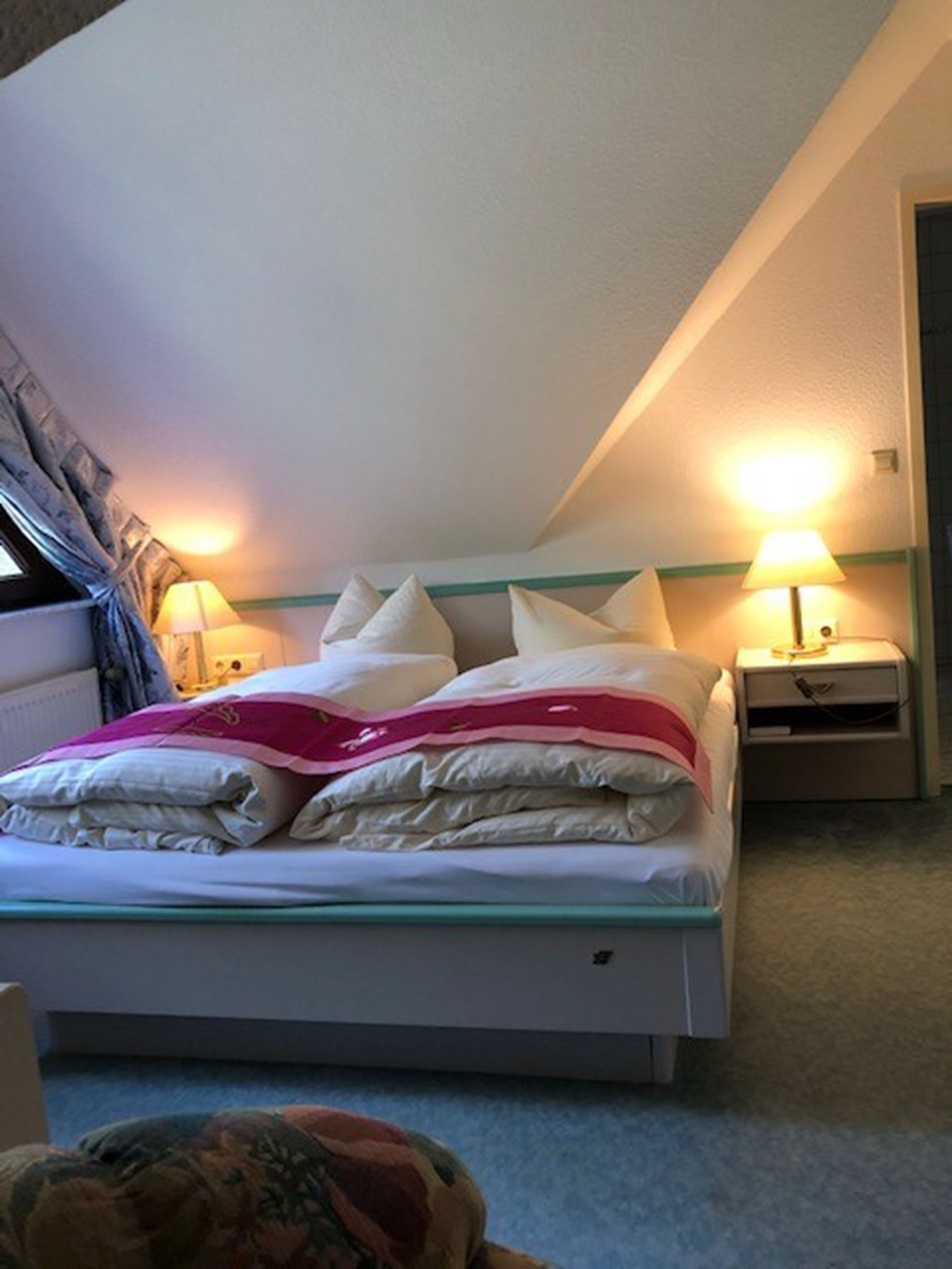 A neatly made bed with pillows and a blanket, two bedside lamps, and a window with curtains.