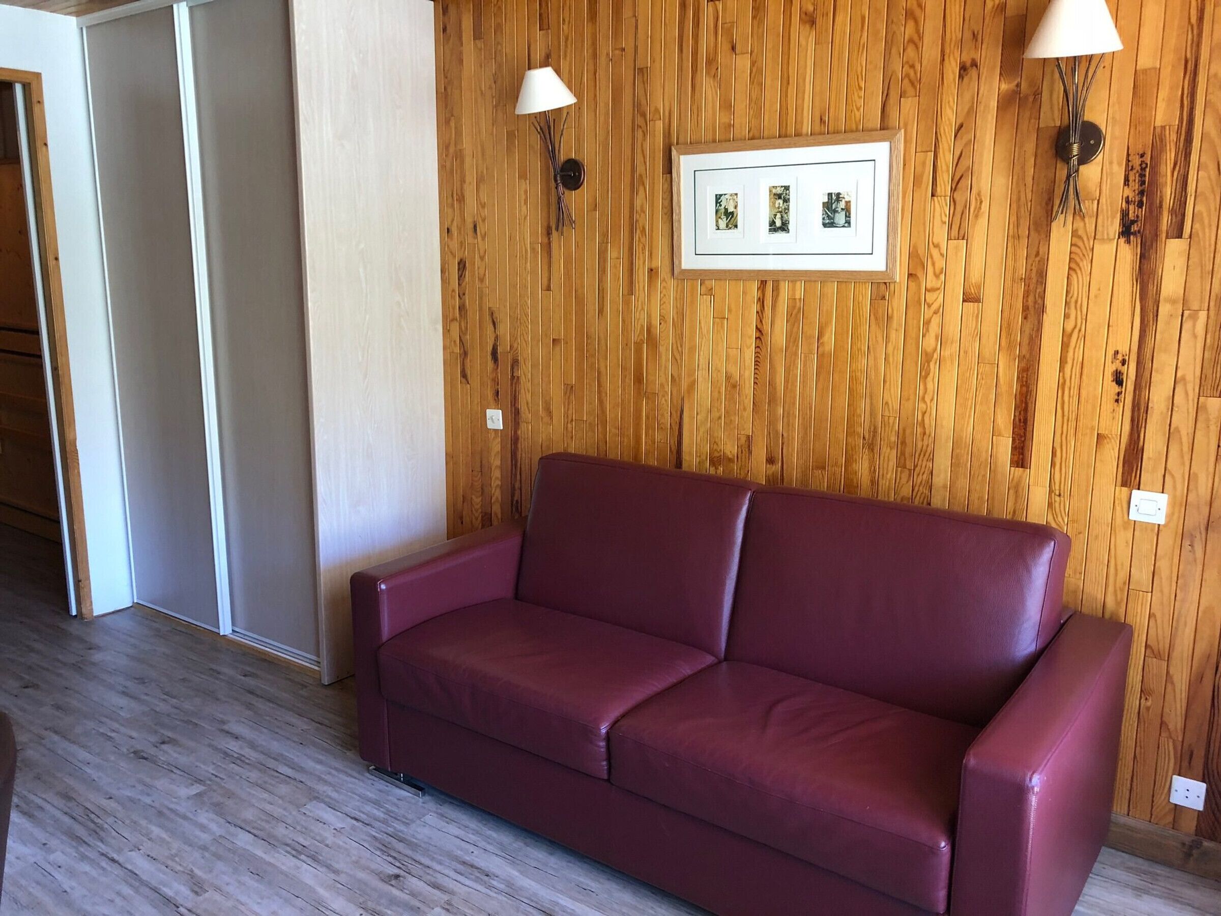 A room with a wooden wall, a framed picture, and a red sofa.