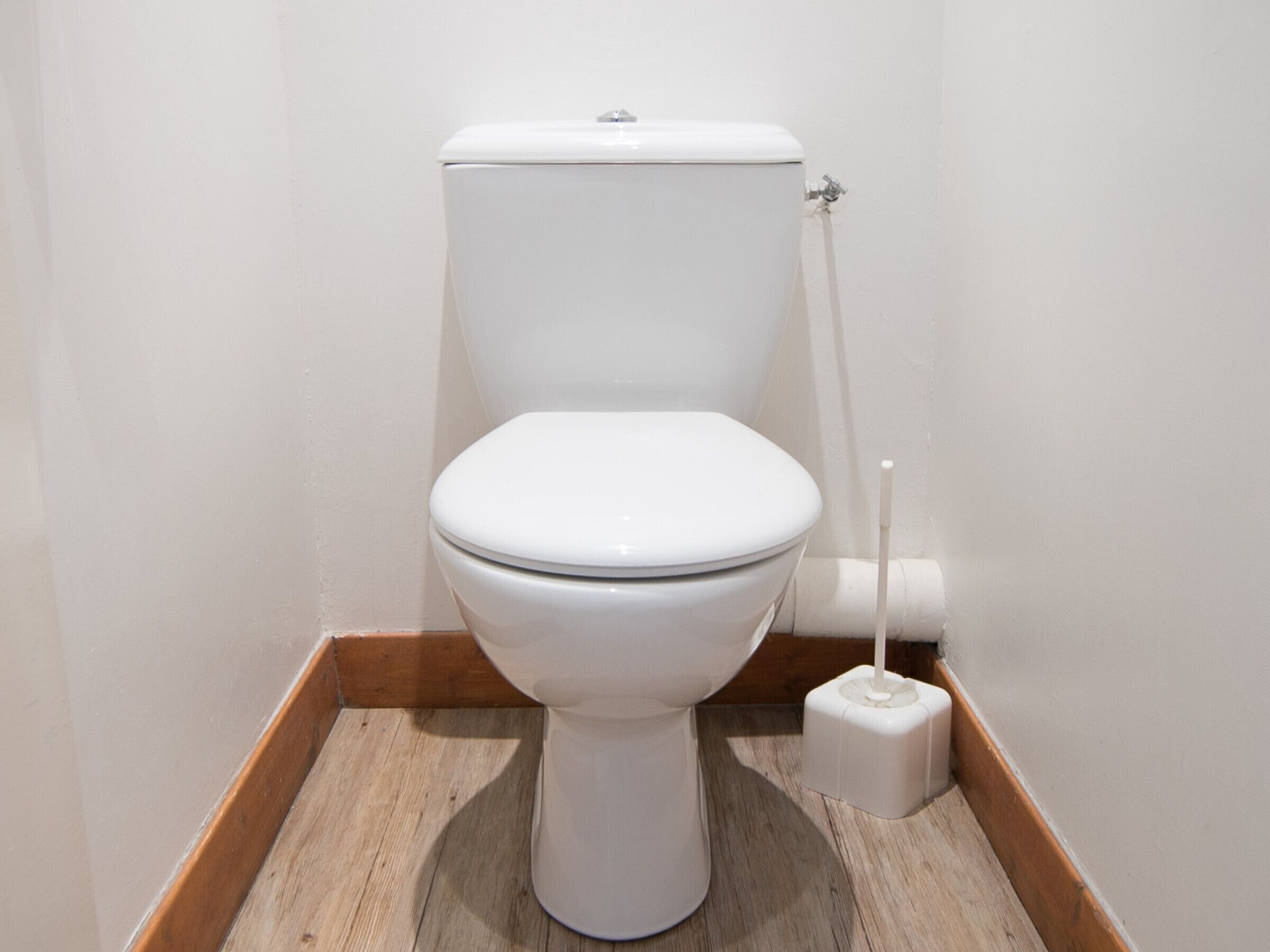 A white toilet in a bathroom with wooden flooring and white walls.