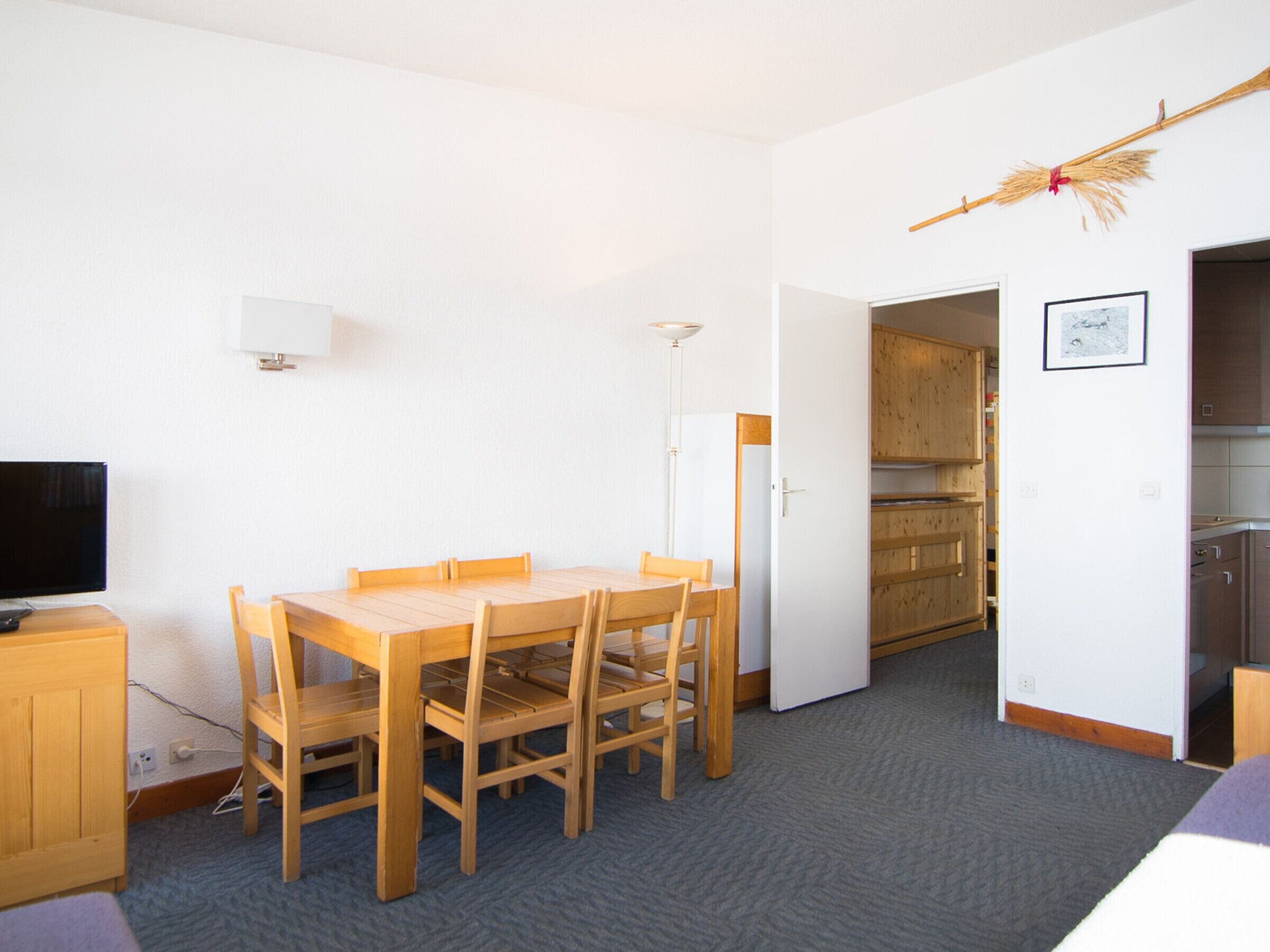 Una habitación compacta con una mesa y sillas de madera, televisión y kitchenette.