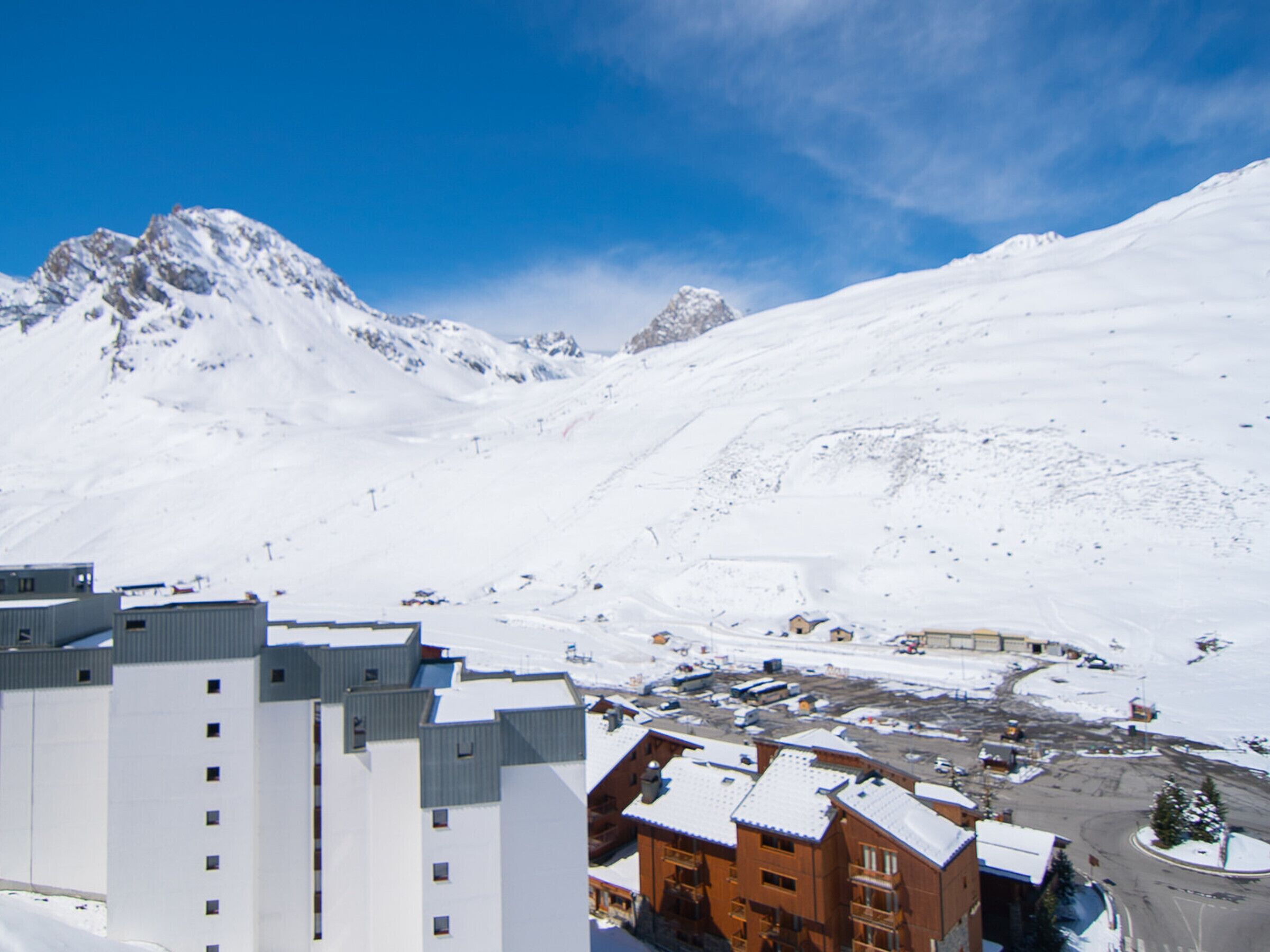 Une ville de montagne enneigée, avec des bâtiments modernes, dont un hôtel avec un télésiège visible en arrière-plan.