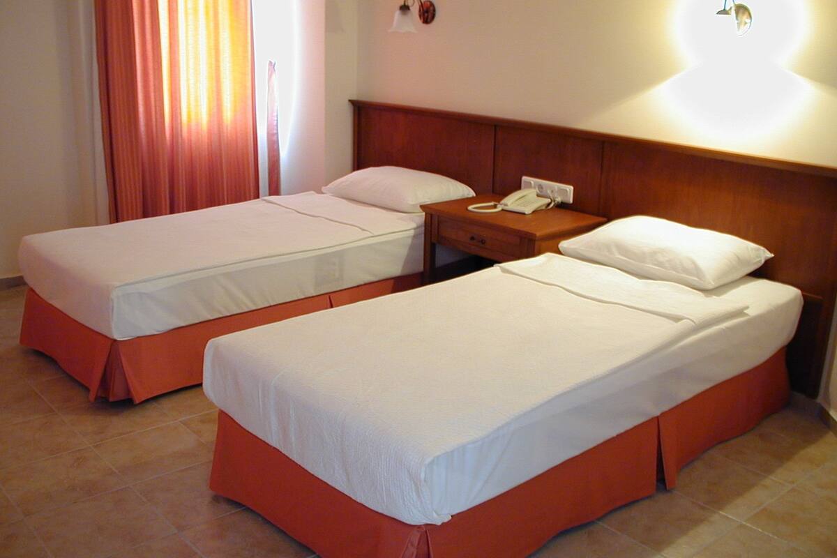 A hotel room with two single beds, a bedside table with a phone, and a wall-mounted light fixture.
