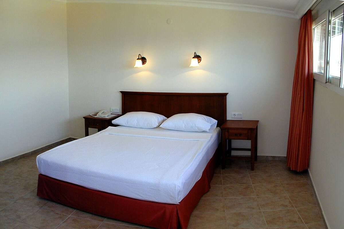A neatly made bed with a wooden headboard, two bedside tables with lamps, and a window with curtains.