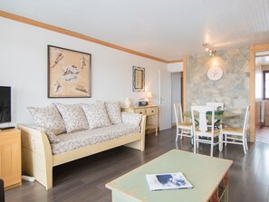 Una sala de estar con sofá, televisor y comedor con sillas y mesa.