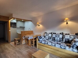 A compact living space with a kitchenette, a sofa with patterned cushions, and a dining area. - South-facing studio 500 m from slopes with Wi-Fi (Tignes)