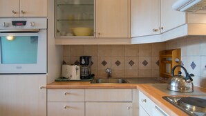 A kitchen with a built-in oven, a coffee maker, a kettle, and a sink.