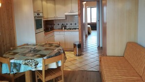 A compact kitchen with wooden cabinets, a dining table with a patterned tablecloth, and a small trash bin.
