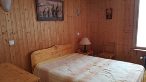 A wooden-paneled room with a bed, a nightstand, a chair, and a wall-mounted lamp.