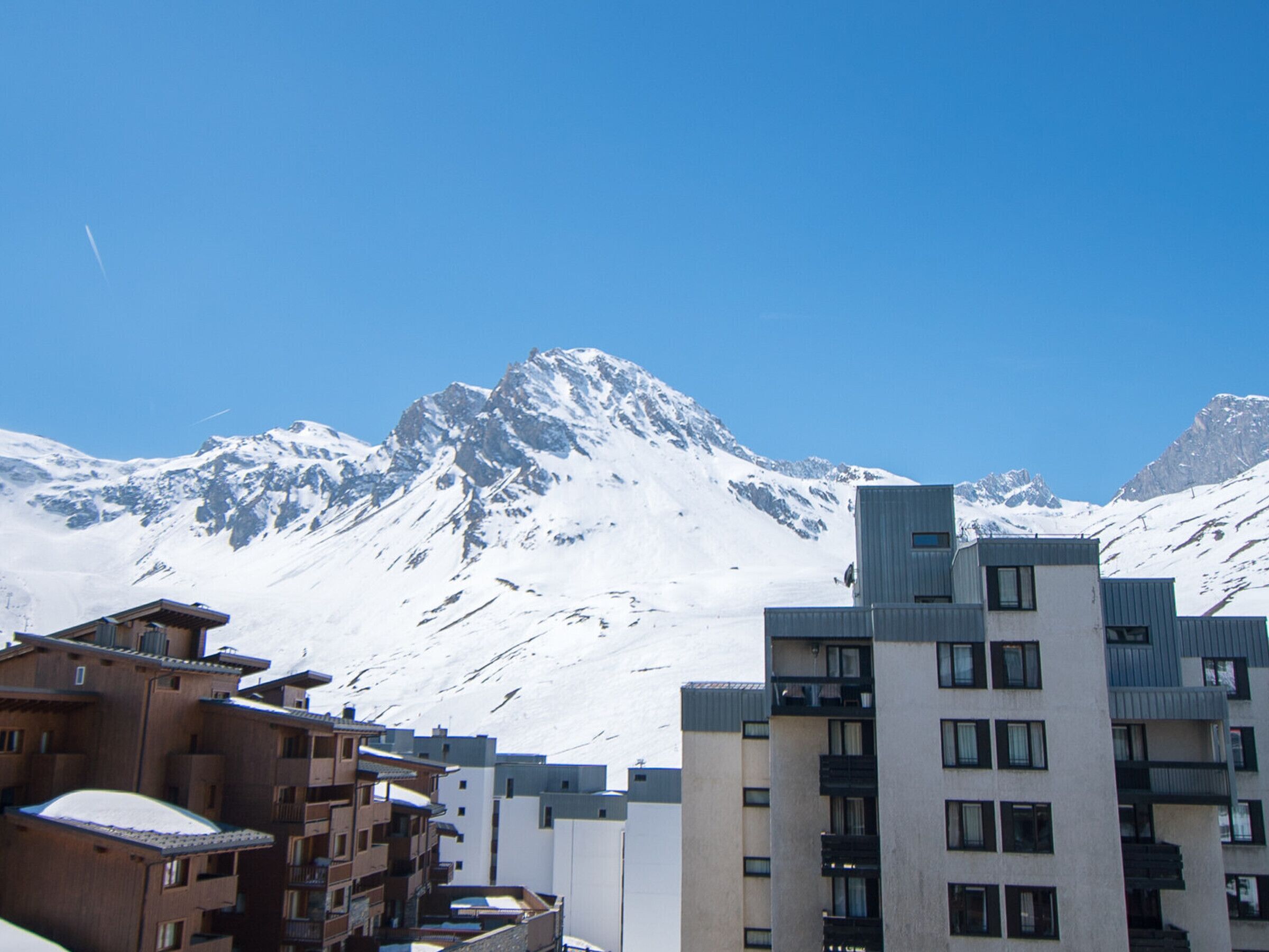 Uma cordilheira com picos cobertos de neve e um edifício moderno com vários andares e varandas.
