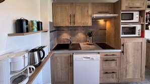 Una cocina compacta con armarios de madera, un lavavajillas Bosch, una cafetera y dos microondas.