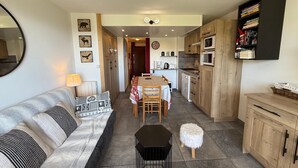 Una sala de estar acogedora con sofá, mesa de comedor y zona de cocina con armarios de madera y microondas.