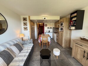 Een gezellige woonkamer met een bank, een eettafel en een keuken met houten kasten en een magnetron.