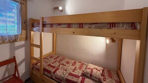 Una cama litera con una escalera, una ventana con cortinas de encaje y una silla de madera.