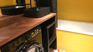 Un baño pequeño con tocador de madera, lavamanos negro, lavadora y bañera.