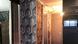 Un pasillo con papel tapiz estampado, una puerta de madera y un electrodoméstico negro, posiblemente un refrigerador u horno.