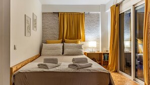A modern bedroom with a large bed, a wooden floor, a brick wall, and a sliding glass door to the right.