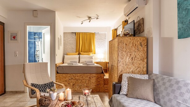 A cozy bedroom with a bed, a wooden wardrobe, a sofa, and a chair.