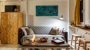 A modern living room with a wooden cabinet, a sofa with patterned cushions, a coffee table with candles and a bowl of fruit, and a teal abstract painting on the wall.