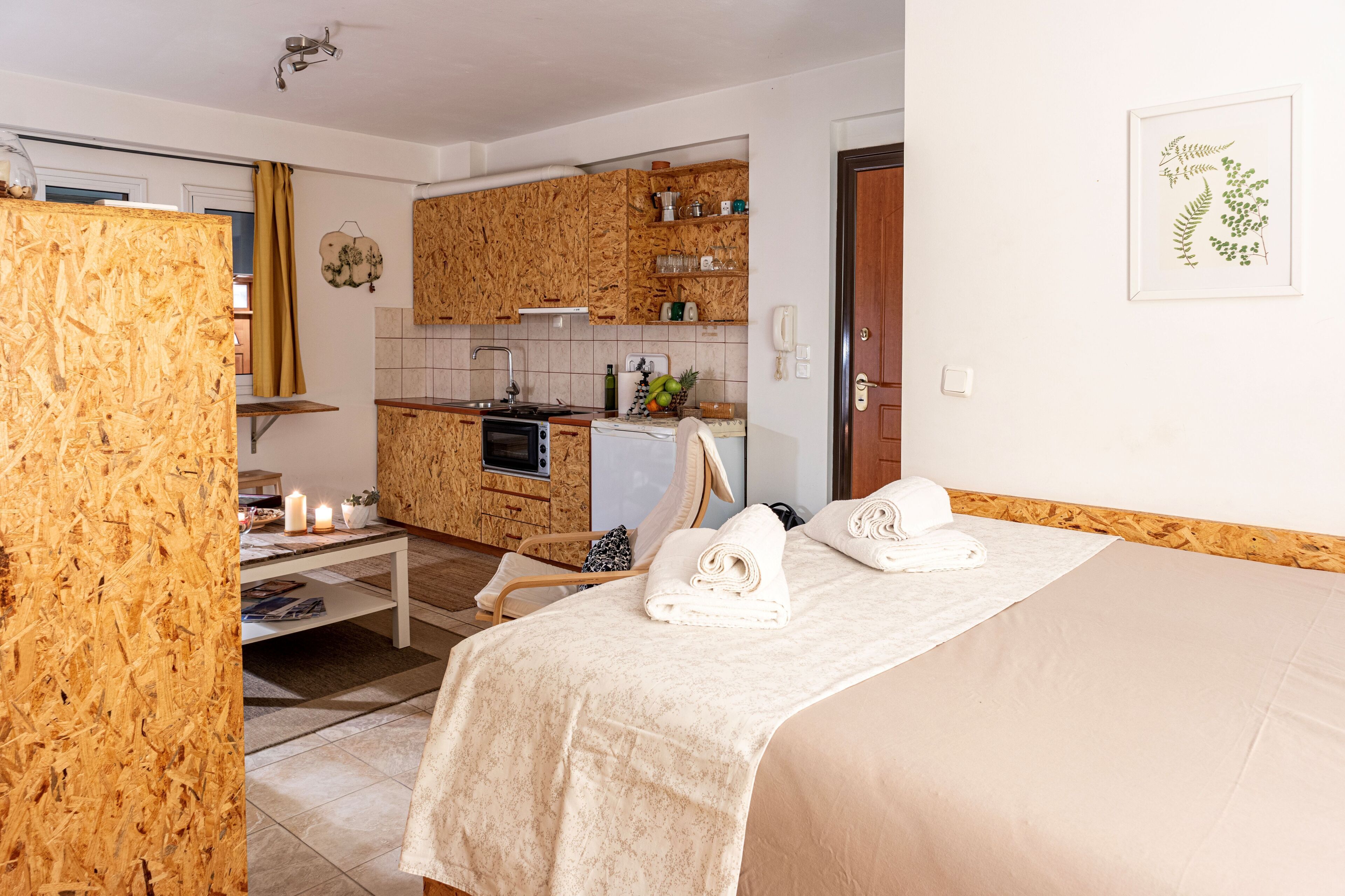 A bedroom with a bed, a bedside table, and a view into a kitchen area.