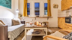 A compact living space with a sofa, a dining table, a small kitchen area with a microwave, and a window with curtains.