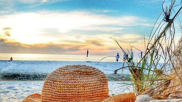A straw hat on a sandy beach with a view of the ocean and people in the distance.