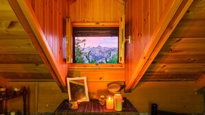 A wooden cabin with a window overlooking a mountainous landscape. Inside, there is a wooden table with a framed picture, candles, and a small decorative item. - Escape in the Forest, Cosy Chalet with Home Cinema (Kalamata)