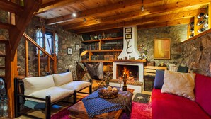 A cozy living room with a fireplace, wooden beams, a red sofa, a white sofa, and a bookshelf. - Escape in the Forest, Cosy Chalet with Home Cinema (Kalamata)