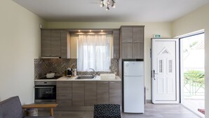 Cocina compacta con electrodomésticos modernos, comedor con un banco, y una puerta corrediza de vidrio que da a un balcón.