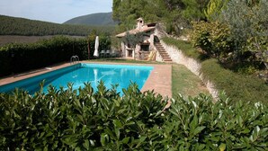 Una piscina rodeada de vegetación exuberante, una escalera de piedra y un edificio rústico con chimenea.