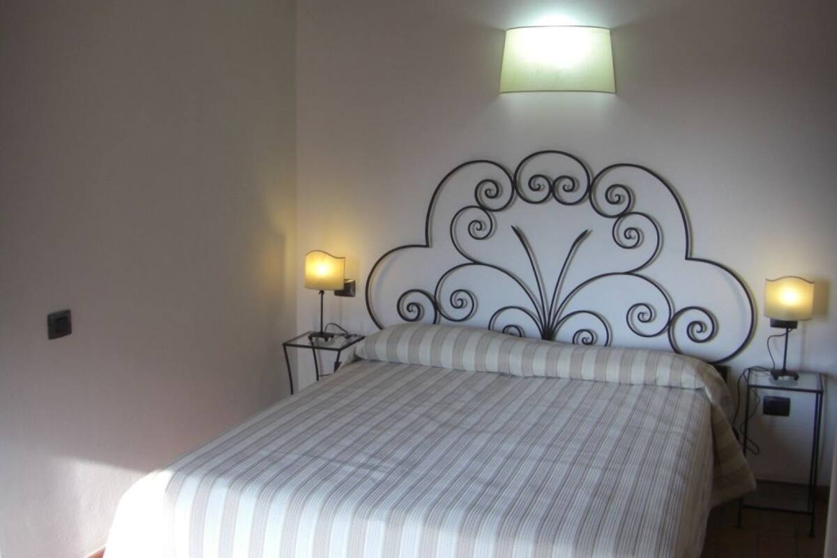 A neatly made bed with a striped bedspread, two bedside tables with lamps, and a decorative wall headboard.