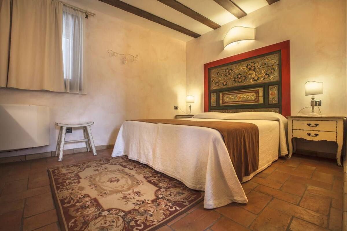 A bedroom with a bed, bedside tables, a radiator, a window with curtains, and a patterned rug.